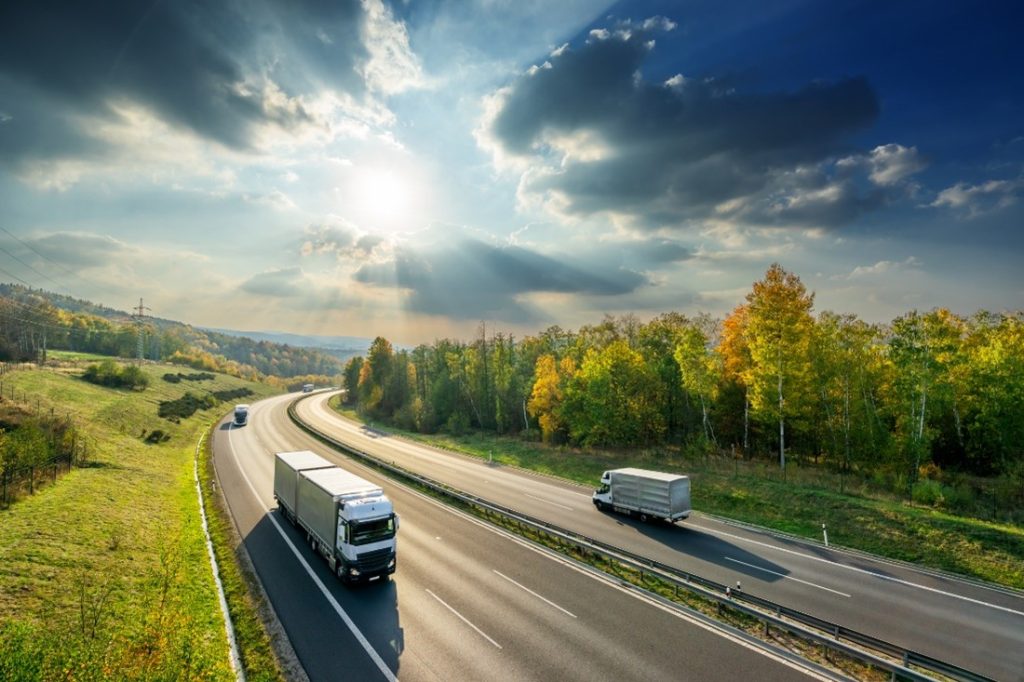 Three lorries are driving down a road on a sunny day